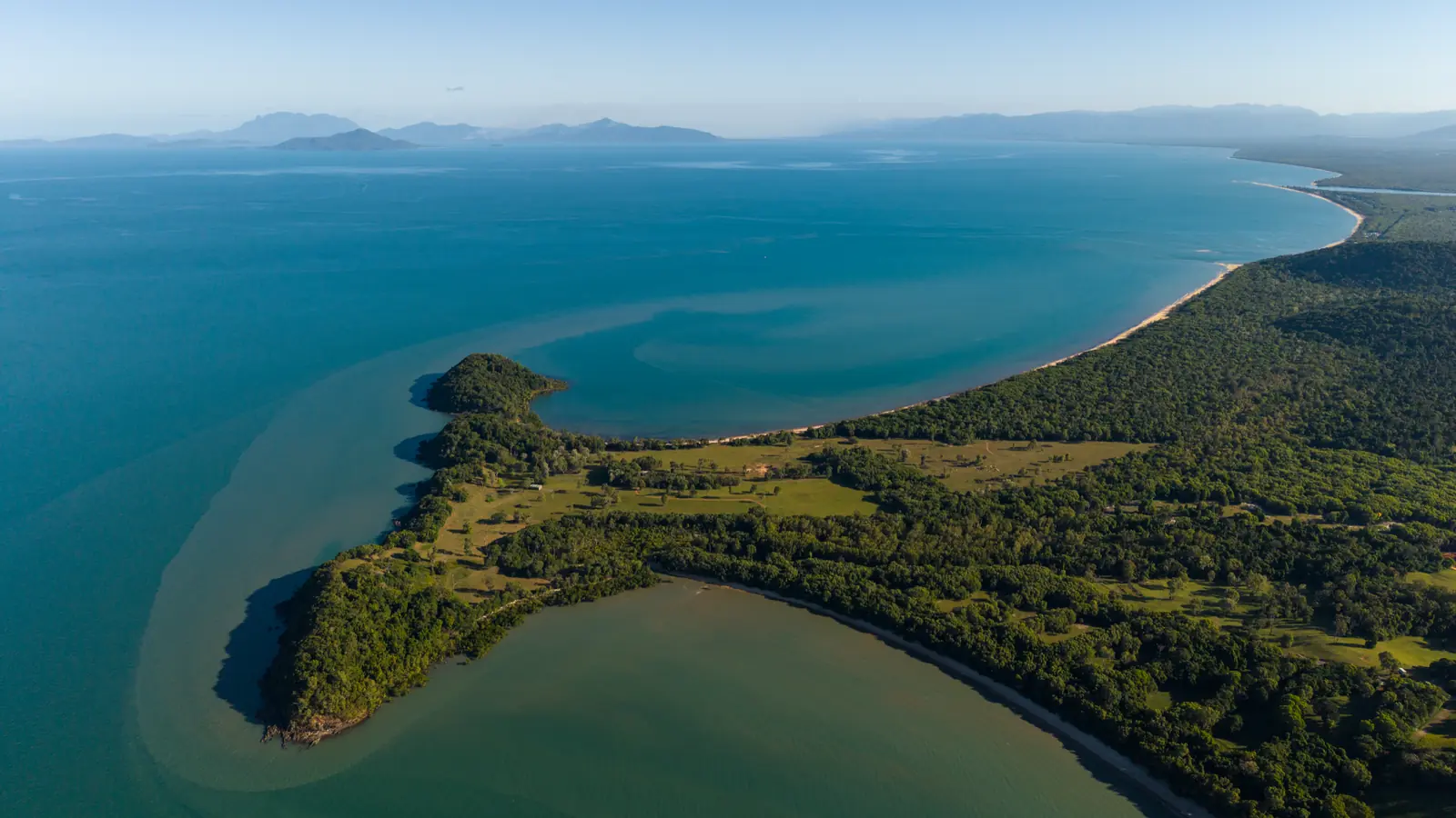 The headland from high over the sea: a wooded point with a bay either side and a long beach running away to the range.