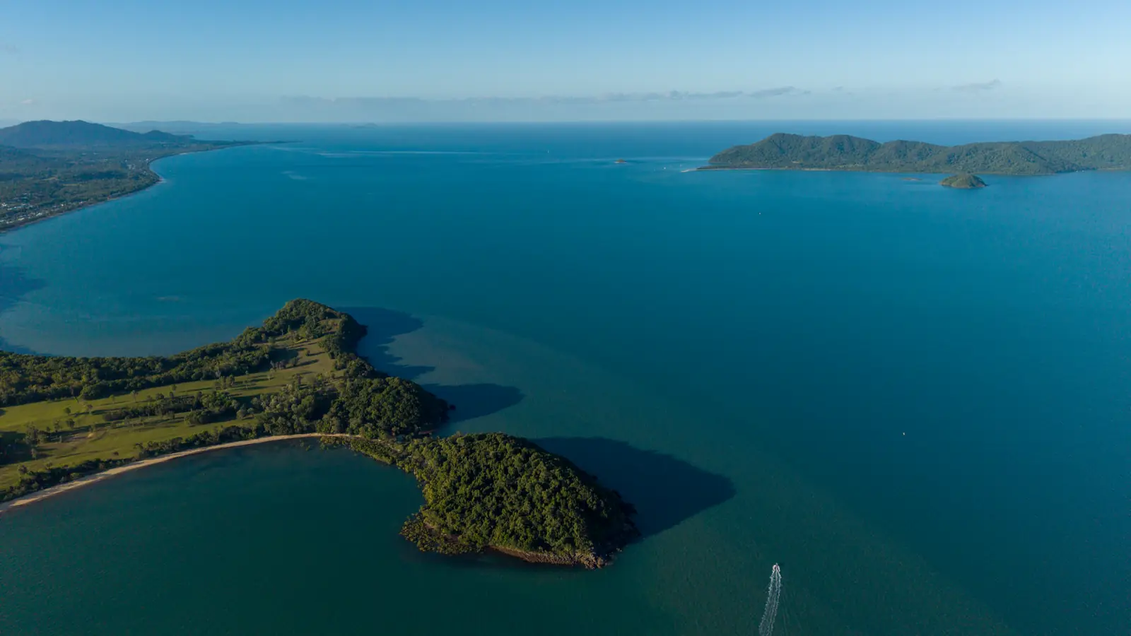 The wooded tip of the headland from above, a boat's wake heading out to sea and an island offshore.