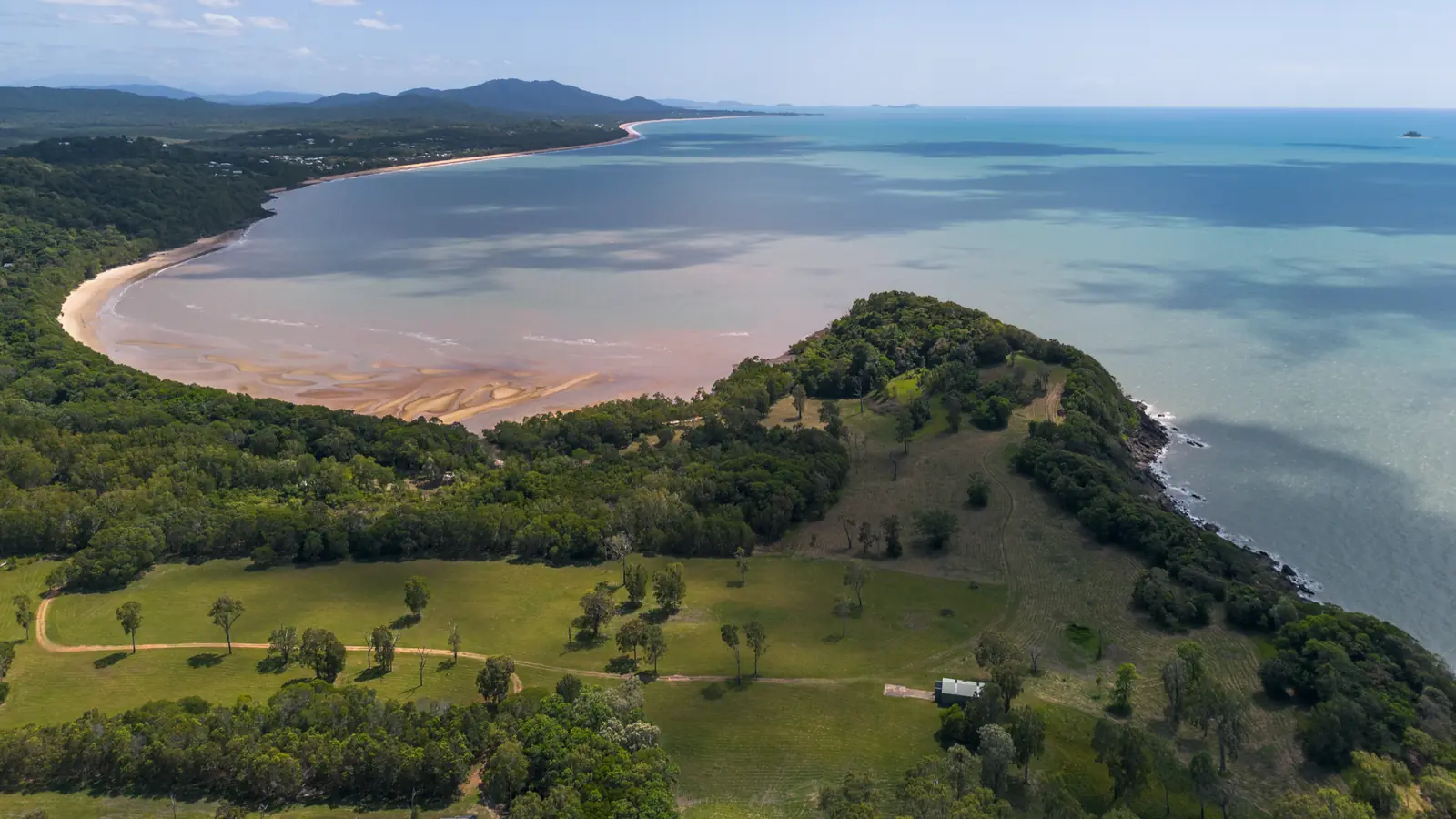 Above the cleared ground on the crest, the bay beside it at low tide in ribbons of sand, the coast running north.
